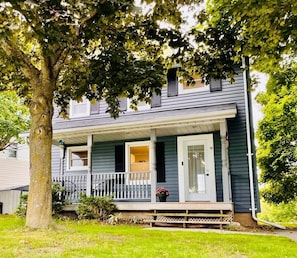 A two-story house with a porch, a visible window, and a door. - The Blue House in the heart of Picton (Prince Edward)
