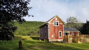 Une maison rouge avec une terrasse en bois et une cour clôturée.