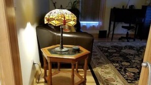 Un escalier menant à un salon où l’on aperçoit une lampe posée sur une table en bois, un tapis à motifs et un tableau accroché au mur.