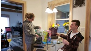 Un coin repas avec une table dressée pour deux personnes, une fenêtre ornée de fleurs et un ventilateur de plafond.