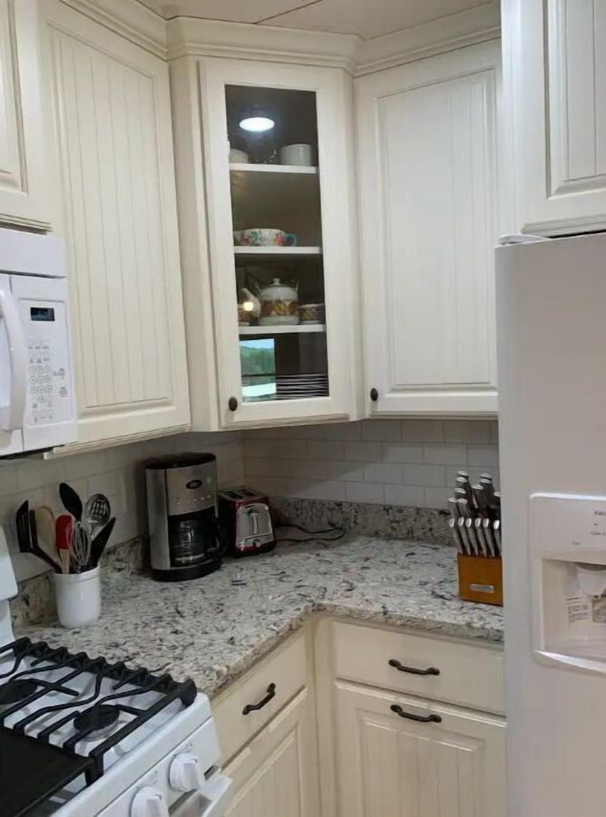 Una cocina con armarios blancos, estufa, cafetera y tostadora.
