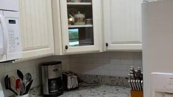 Una cocina con armarios blancos, estufa, cafetera y tostadora.