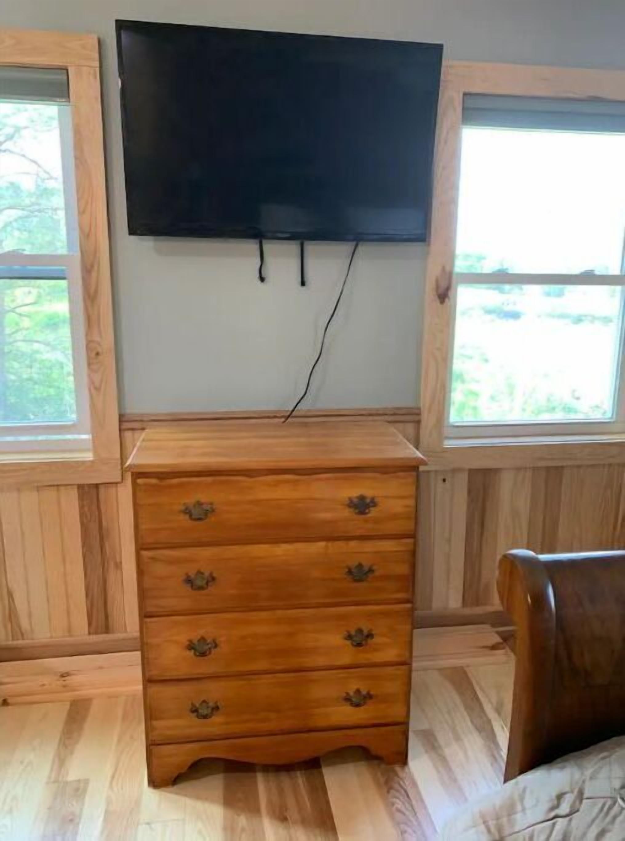 Una habitación con un aparador de madera, un televisor de pantalla plana montado en la pared y ventanas con vistas al verdor.