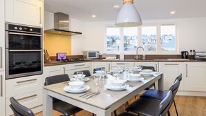 A modern kitchen with white cabinets, a double oven, and a dining area set for six with a table and chairs. - Seaview (Dartmouth)