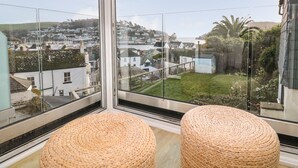 A balcony with wicker ottomans, a glass railing, and a view of a coastal town. - Seaview (Dartmouth)