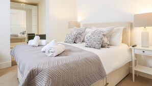 A neatly made bed with rolled towels, a headboard with decorative pillows, bedside lamps, and a small white nightstand. - Seaview (Dartmouth)