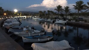 A marina with boats docked, palm trees, and a calm water body reflecting the sky. - Aquamarina Pintadera Rossa & SPA (Porto Pino)