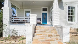 A white building with a blue door, stone steps, and a porch with a bench. - Charming home, downtown Mineral Wells (Mineral Wells)