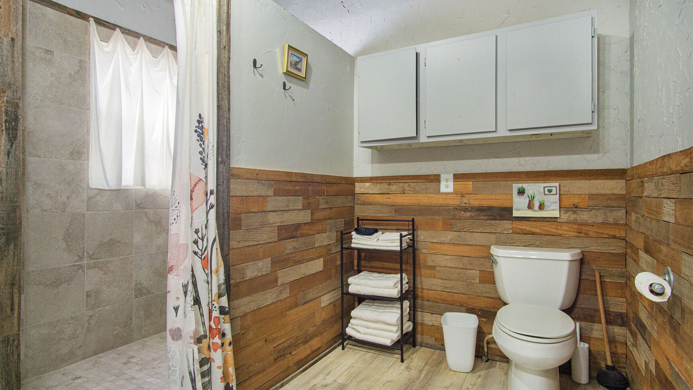 A bathroom with a wooden wall panel, a toilet, a shelf with folded towels, and a shower curtain.