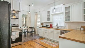 A modern kitchen with white cabinetry, a wooden countertop, and a dining area with chairs. - Charming home, downtown Mineral Wells (Mineral Wells)
