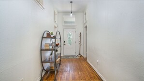 A hallway with wooden flooring, a white door with a glass window, and a metal shelf with books and plants. - Charming home, downtown Mineral Wells (Mineral Wells)
