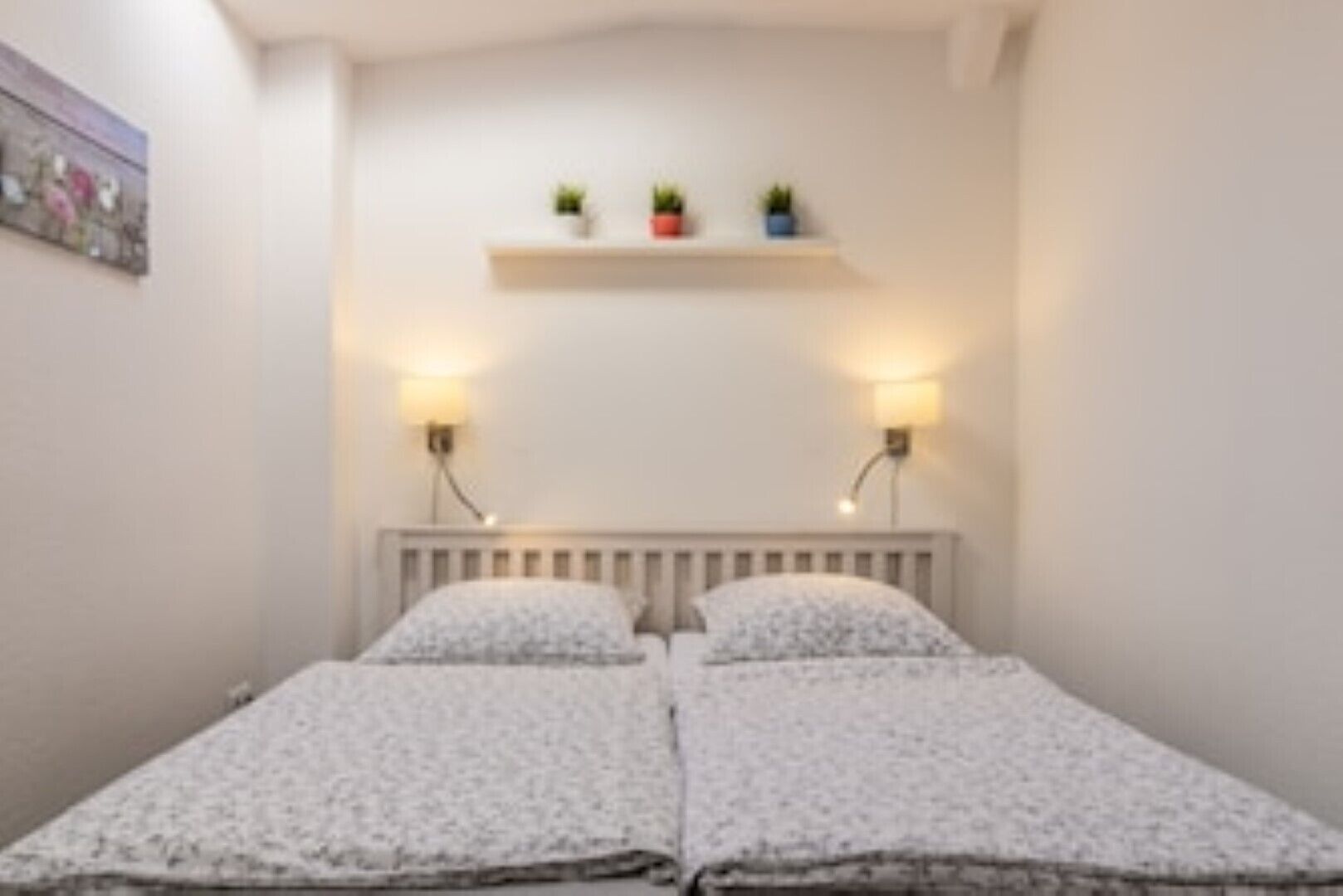 A bedroom with two beds, a white headboard, and two wall-mounted lamps.