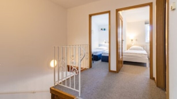 Hotellihuoneessa on sänky, yöpöytä ja peili. Huoneesta johtaa toiseen huoneeseen portaat, joissa on kaide.