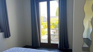 Une chambre à coucher avec un lit, une porte-fenêtre coulissante donnant sur un jardin et un miroir au mur.