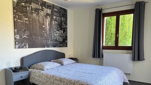 Une chambre à coucher comprenant un lit, une table de chevet, une lampe, une fenêtre avec des rideaux et un tableau représentant un paysage urbain accroché au mur.