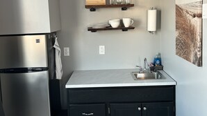 Una cocina con un refrigerador de acero inoxidable, gabinetes negros, encimeras de mármol y un fregadero. Hay estantes de madera sobre la encimera con utensilios de cocina y vasos.