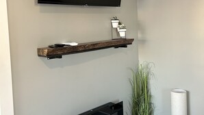Una sala de estar moderna con televisor de pared, chimenea y una pequeña estantería con adornos.
