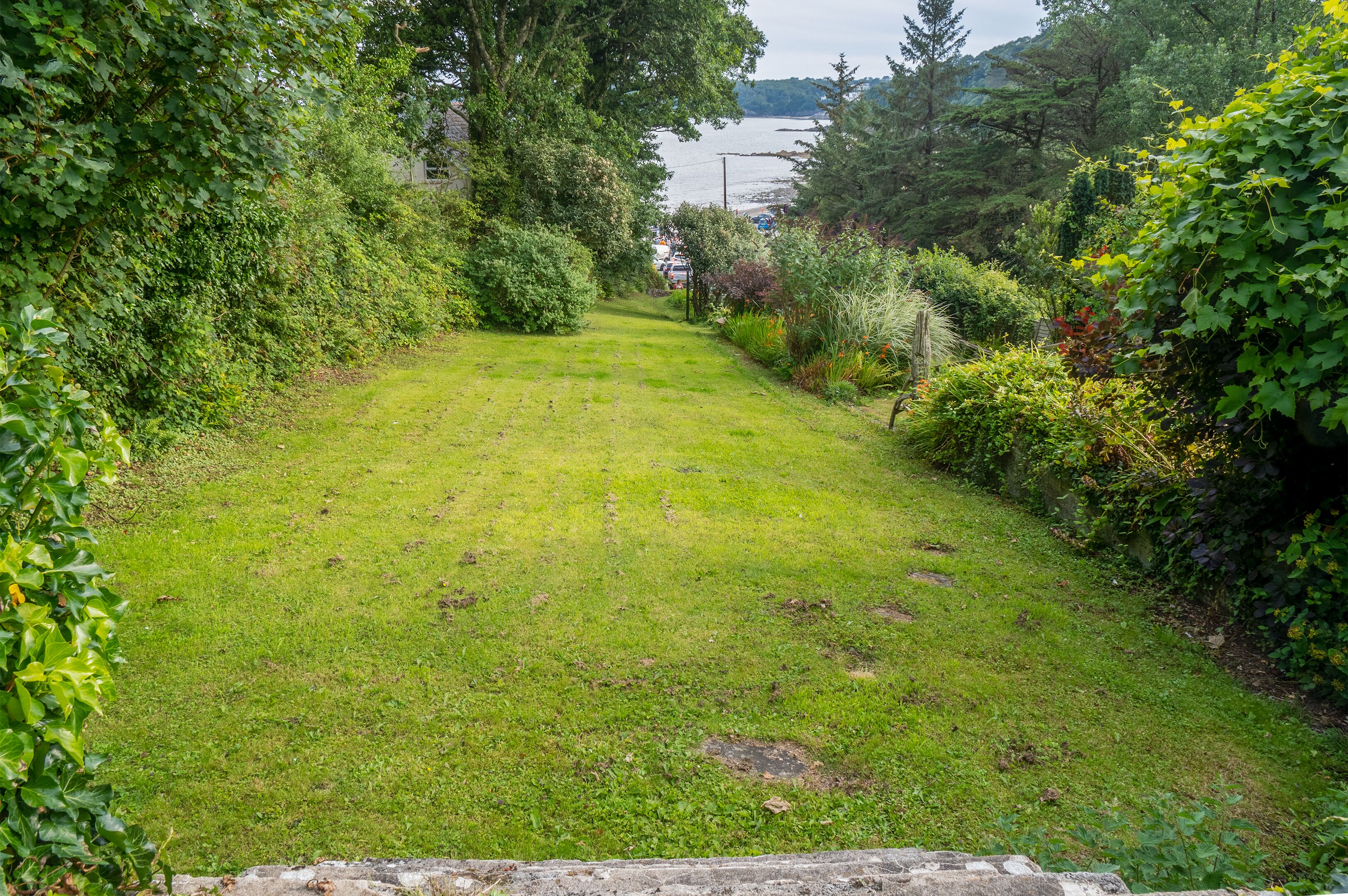 A well-maintained grassy pathway flanked by dense foliage and a body of water in the background.