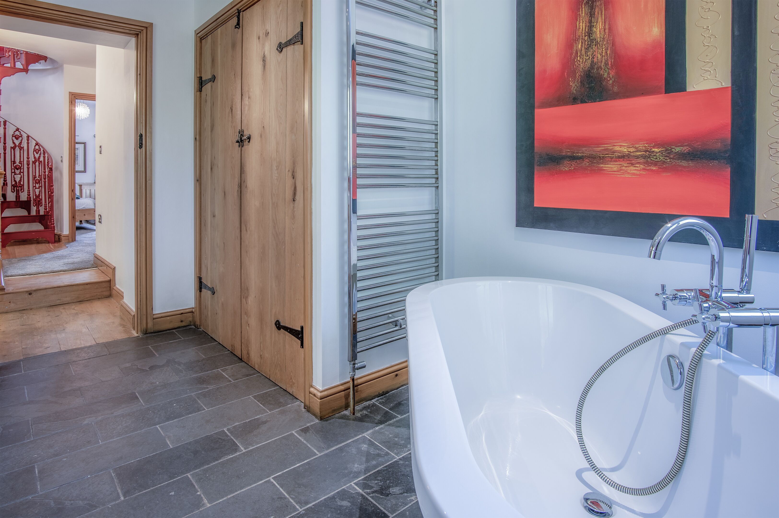 A modern bathroom with a large bathtub, a wooden door, and a radiator.