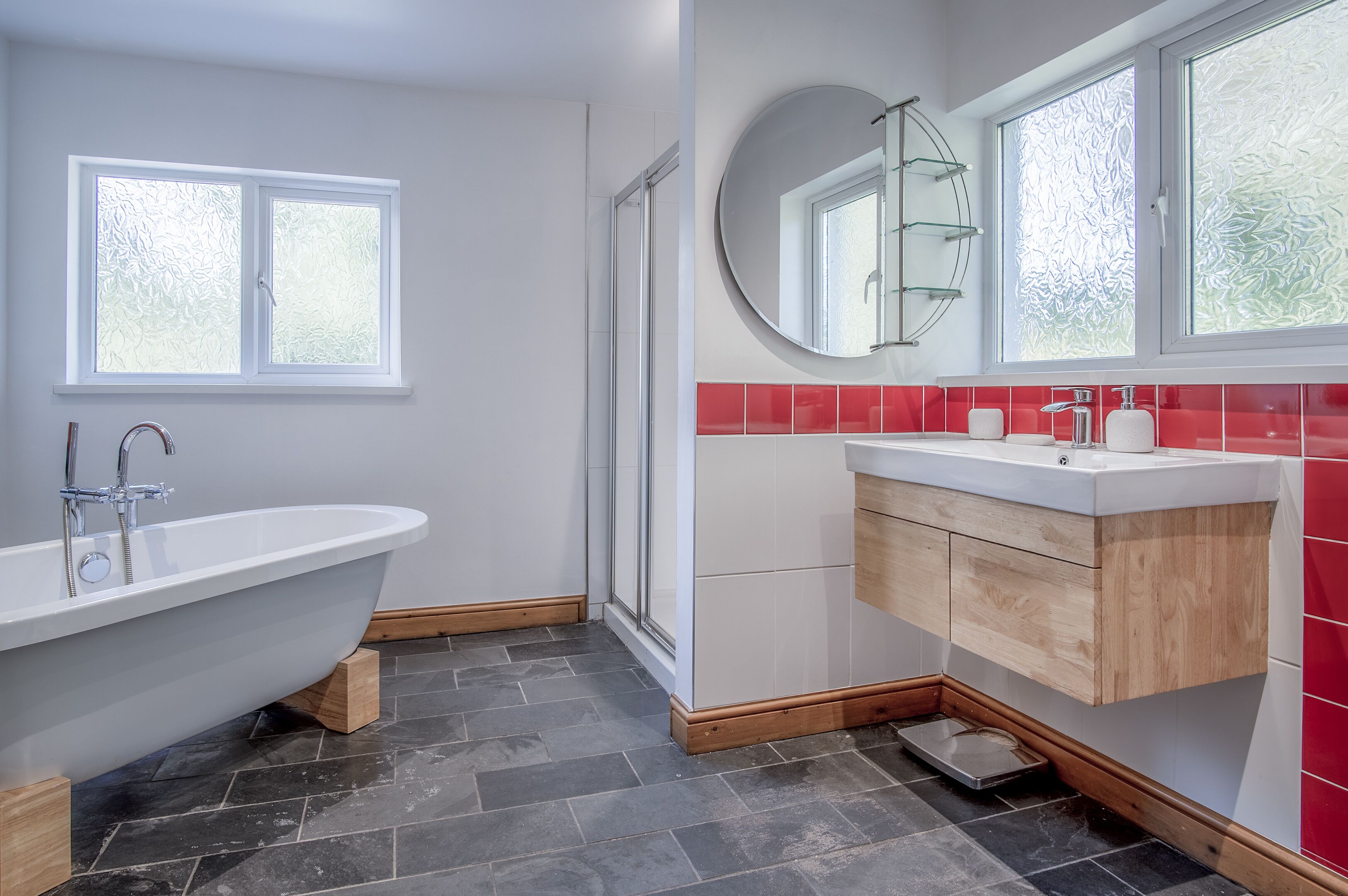 Un baño moderno con una bañera independiente, cabina de ducha de vidrio, tocador con espejo y paredes de azulejos rojos.