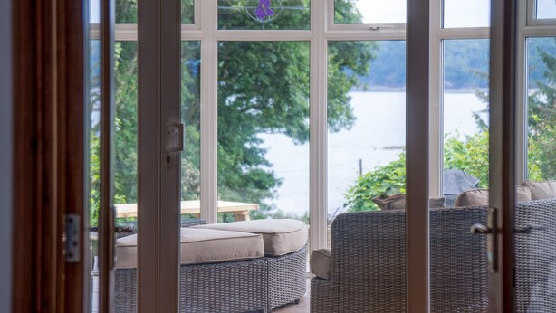 A view through a glass door to an outdoor seating area with wicker furniture and a view of a lake.
