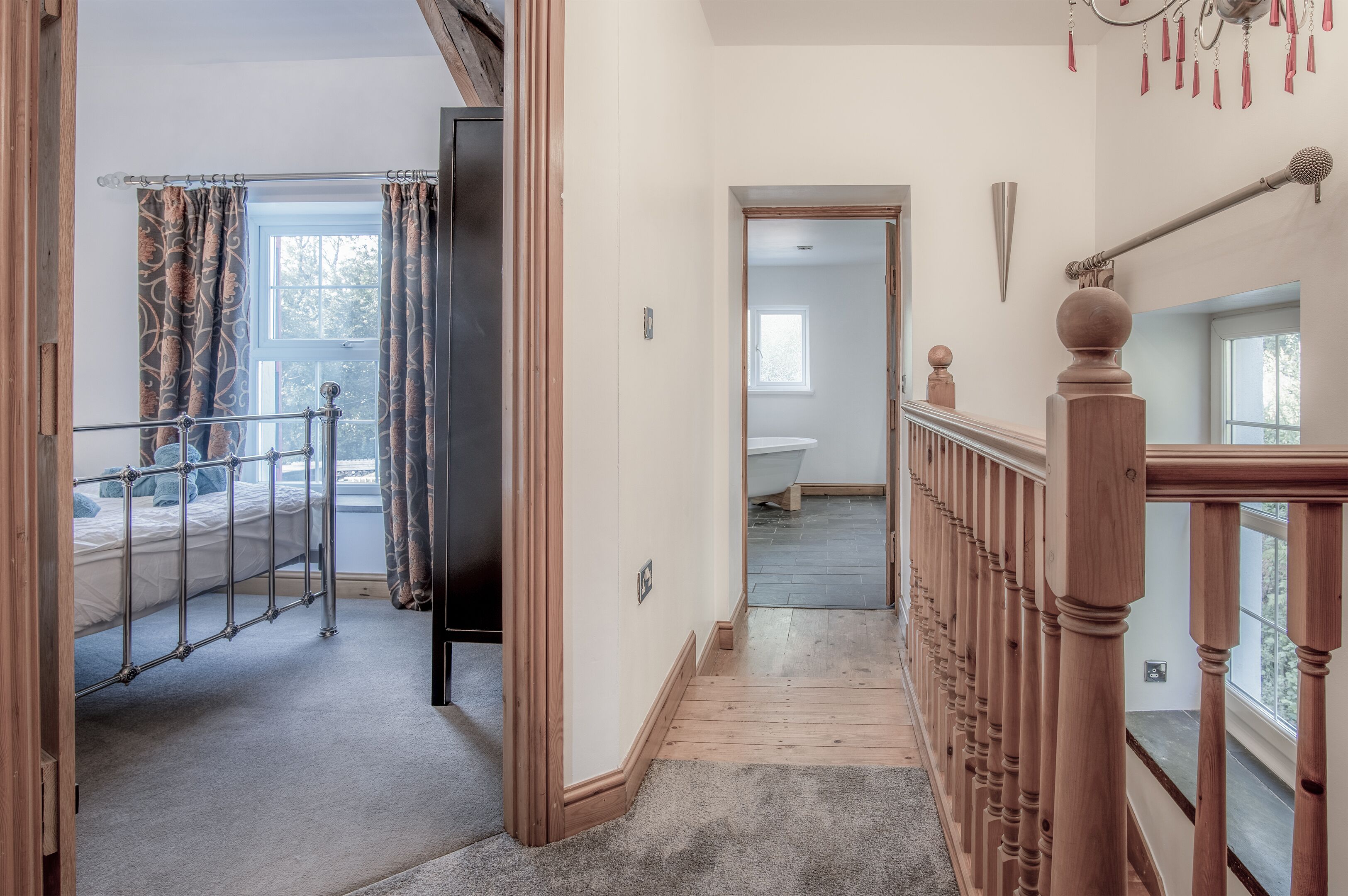 A hallway with a wooden railing, a metal bed frame, and a carpeted floor.