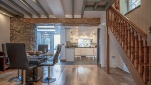 A spacious dining area with a stone wall, a wooden staircase, and a view into the kitchen.