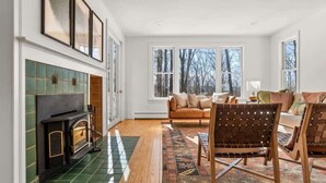 A spacious living room with a fireplace, large windows, and a cozy seating area. - Hupi House: A Peaceful, Wooded, Lakeside Sanctuary (Monterey)