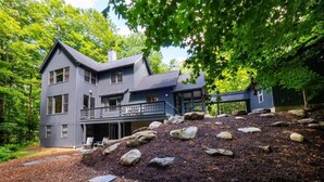 A two-story house with a balcony, surrounded by a wooded area and a pile of mulch. - Hupi House: A Peaceful, Wooded, Lakeside Sanctuary (Monterey)