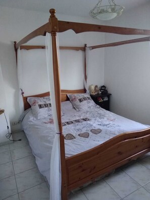 Uma cama de dossel com cortina, roupa de cama branca com desenhos de coração e uma pequena mesa de cabeceira com figuras.