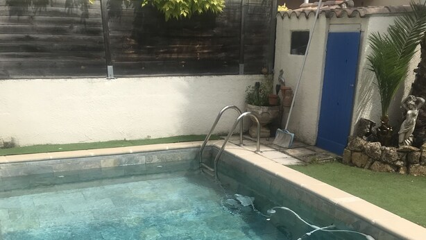 Una piscina con agua azul cristalina, suelo de baldosas y una puerta azul al fondo.