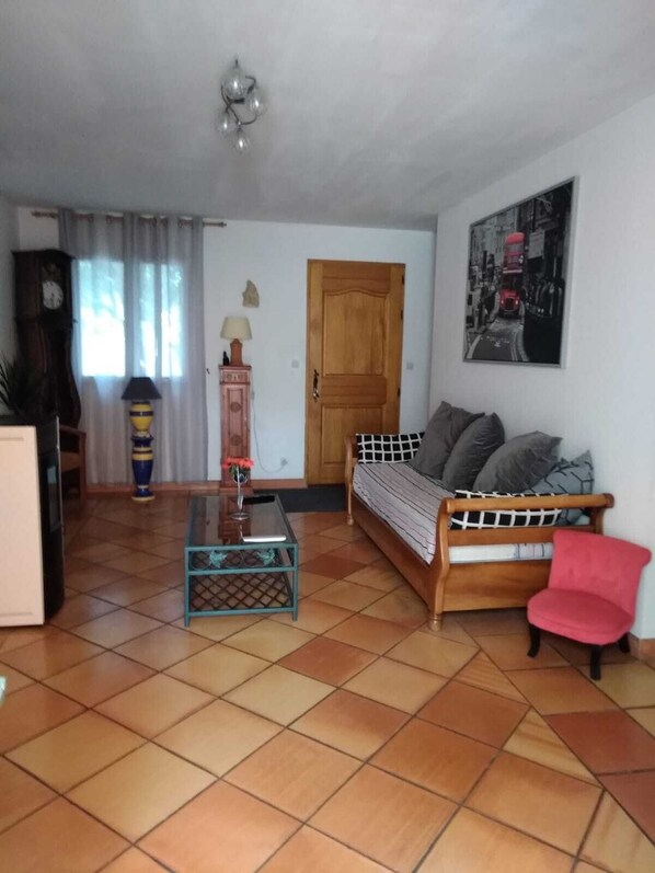 Uma sala de estar com sofá, mesa de centro, uma poltrona vermelha, relógio, abajur e porta.