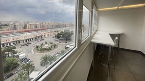A room with a large window overlooking a cityscape, a white desk, and a chair. - SkyLine (Bari)