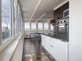 Eine moderne Küche mit großen Fenstern, einem Edelstahlbackofen und einem Essbereich mit Stühlen.
