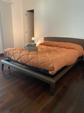 Ein ordentlich bezogenes Bett mit einem Holzrahmen und einer orangefarbenen gesteppten Decke.