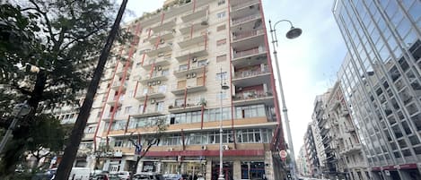 A multi-story residential building with balconies, a ground-level commercial space, and a parking area.