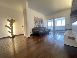 Ein geräumiges Wohnzimmer mit Holzboden, einem schwarzen Ledersofa, einem weißen Heizkörper und einem Stadtbild an der Wand.