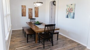 Uma sala de jantar com uma mesa de madeira, quatro cadeiras, um banco, um lustre e um quadro na parede.