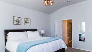 Quarto com cama, mesa de cabeceira, abajur e duas obras de arte floral emolduradas na parede.