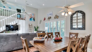 A dining area with a wooden table and chairs, a grey sofa, and a staircase in the background. - House at Bonita (Bonita Springs)