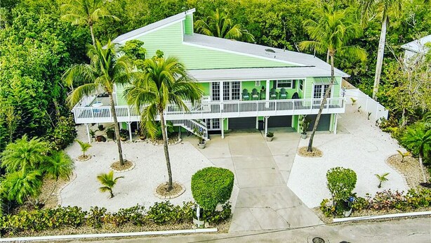 A green building with a white porch, surrounded by palm trees and greenery. - House at Bonita (Bonita Springs)