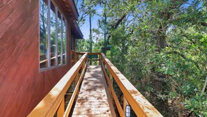 Une terrasse en bois mène à un chalet doté de grandes fenêtres, le tout étant entouré d’une forêt dense.