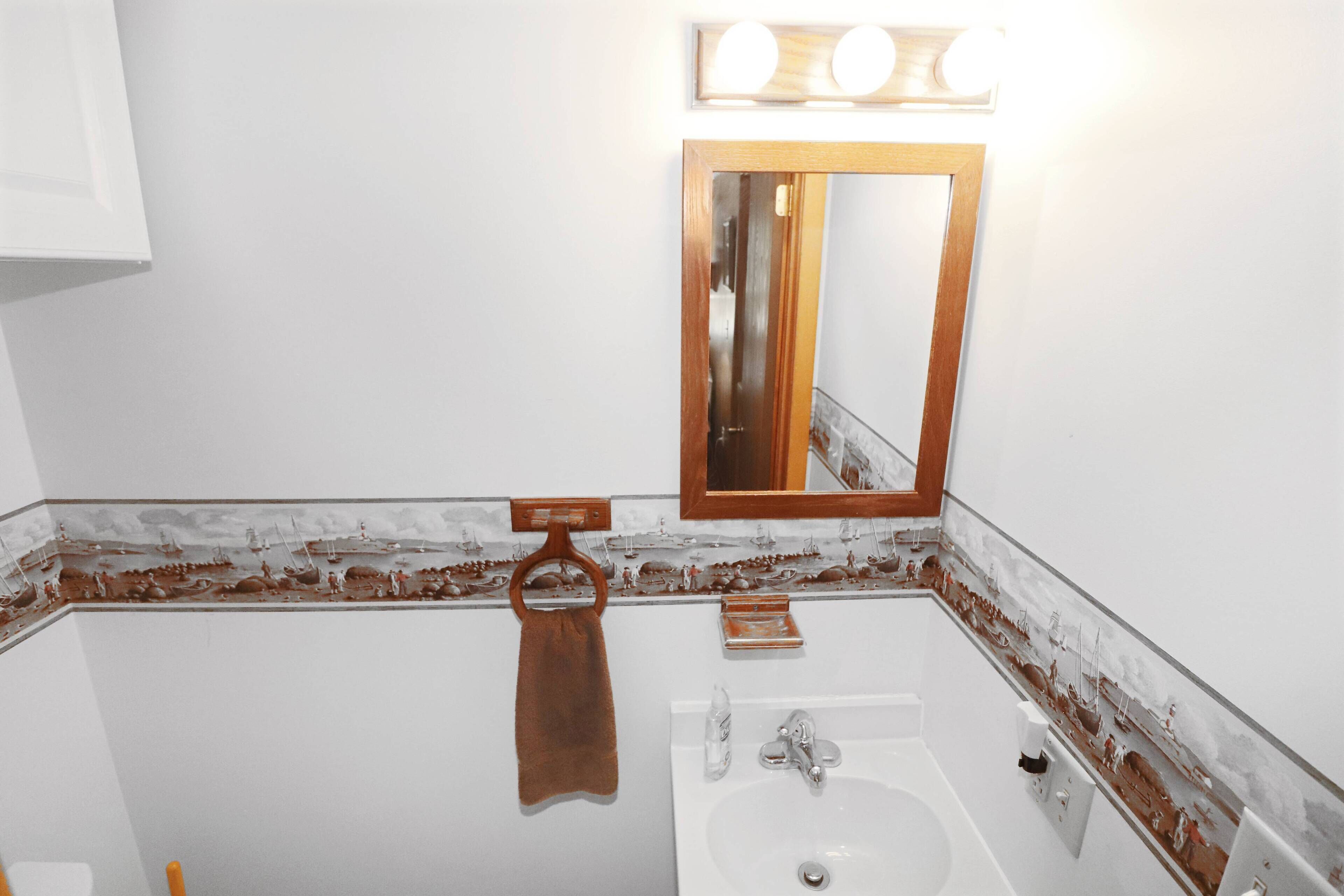 Une salle de bain avec un lavabo blanc, un porte-serviettes en bois et un miroir avec un cadre en bois.