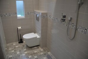 A small bathroom with a toilet, a shower, and patterned tiles. - The Annexe @ Woodland (Bury)
