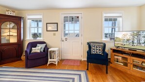 A living room with a wooden cabinet, a purple armchair, a blue armchair, a white side table, and a television.