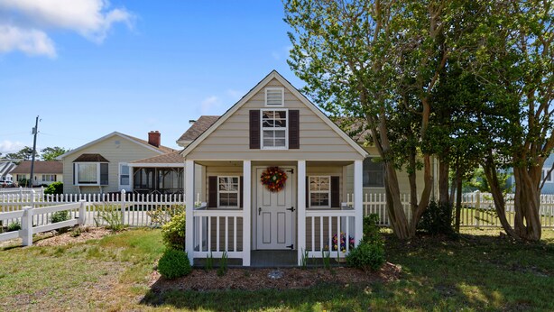 A single-story house with a front porch, a decorative wreath, and a white picket fence.