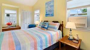A bedroom with a striped bedspread, a painting of a bird, and a lamp on a nightstand.