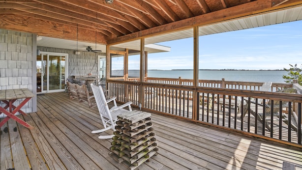 Une terrasse en bois offrant une vue sur l’eau, un espace salon abrité et une pile de planches de bois.