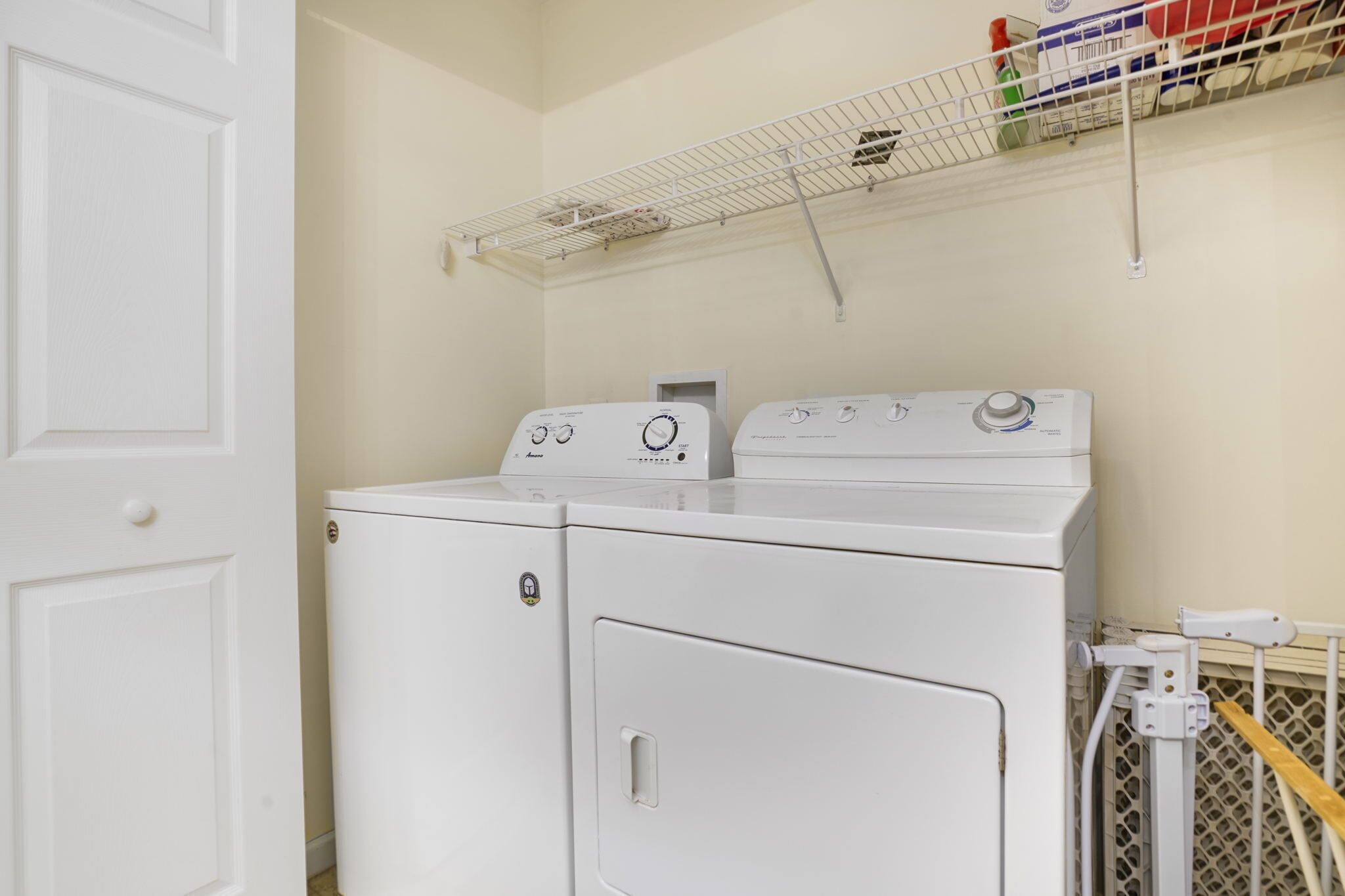 Un espace buanderie avec deux machines à laver et deux sèche-linge superposés, une étagère en métal au-dessus et une porte blanche.