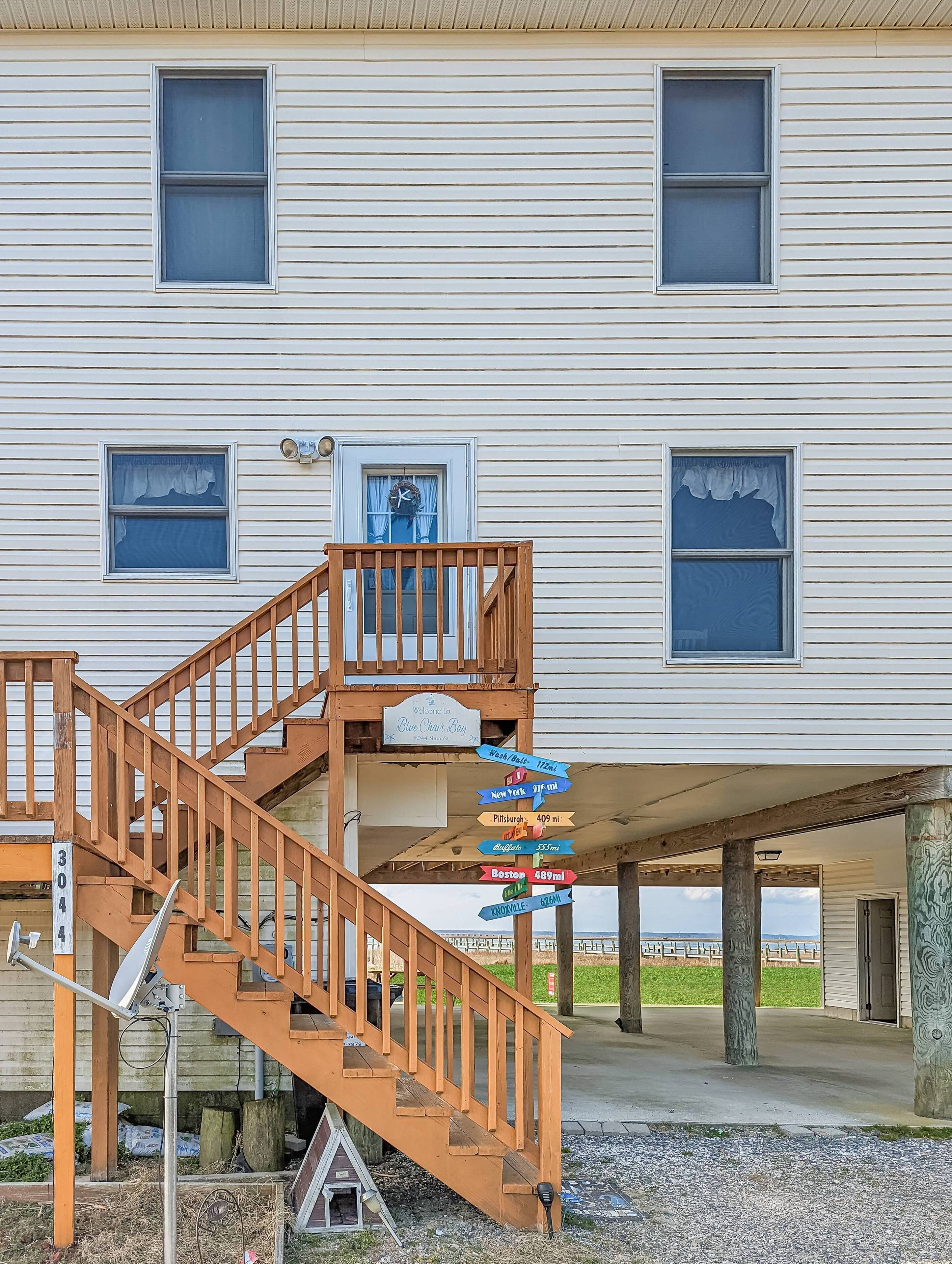 A two-story house with a wooden staircase leading to a balcony. There is a sign with distances to various cities.